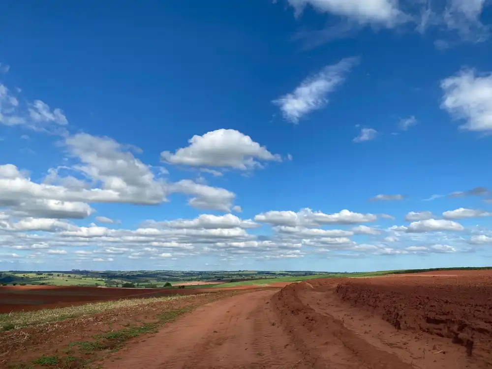 Estrada de terra vermelha no campo, sob céu aberto.